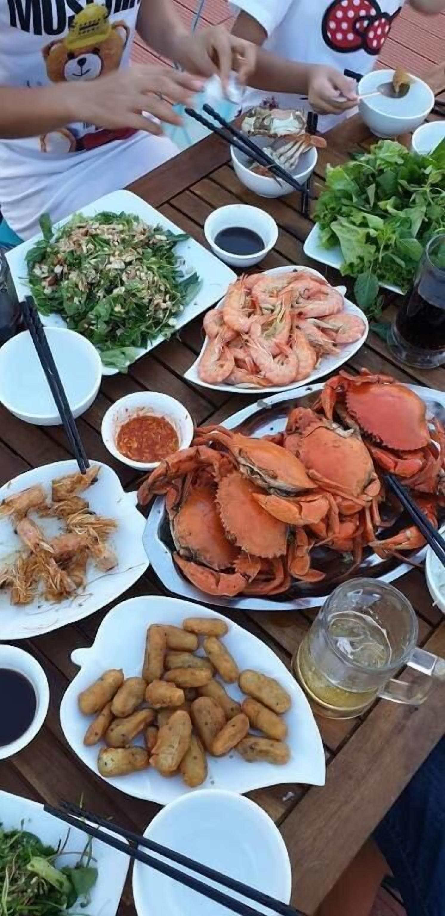 A dining table with various seafood dishes, including shrimp, crab, and fried items, along with bowls of sauces and greens.