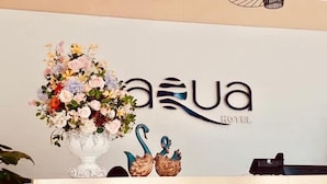 A reception desk with a floral arrangement, a logo for 'Aqua Hotel', and two decorative swans. - Aqua Resort Hai Tien - by BAYLUXURY (Hoang Tien)