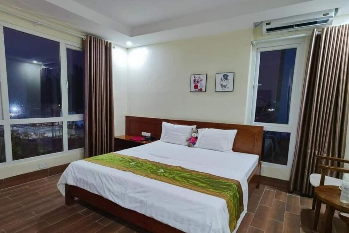 A hotel room with a large bed, a nightstand, a chair, and a window with curtains.