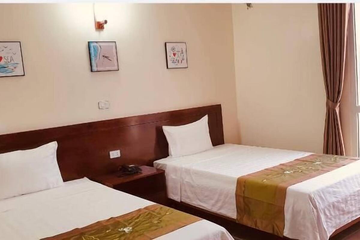 A hotel room with two single beds, a wooden headboard, a nightstand, and a window with curtains.