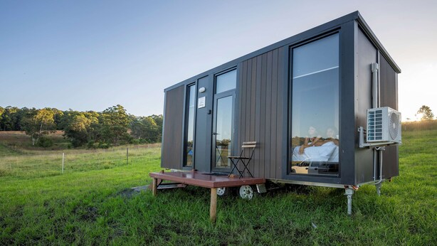 A modern, compact cabin with a sliding door, a small deck, and an air conditioning unit. - The Fog Getaway 2 by Tiny Away (Boolambayte)