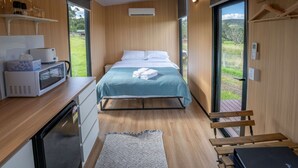 A bedroom with a bed, a desk with a microwave, a refrigerator, and a view of the outdoors. - The Fog Getaway 2 by Tiny Away (Boolambayte)