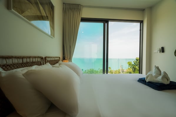 Habitación de hotel con una cama grande, vista al mar a través de una puerta corrediza de vidrio y un balcón con vistas a la ciudad.