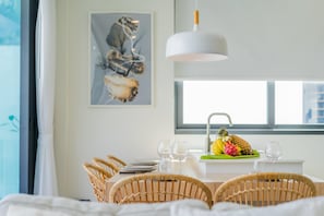 Un comedor con una mesa dispuesta para dos, sillas de mimbre, una lámpara colgante blanca y una ventana con vistas.