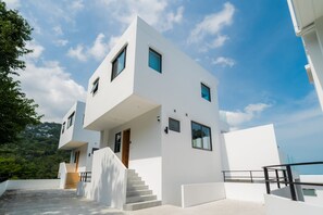 A modern white building with a staircase leading to a wooden door, surrounded by a white balcony and a clear sky.