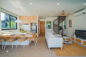 Eine moderne Küche mit Essbereich, ein Wohnzimmer mit Sofa und Fernseher sowie eine Wendeltreppe.