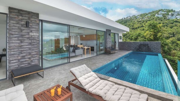 Una casa moderna amb un porxo de vidre, una piscina i vistes a un vessant de turons verdós.
