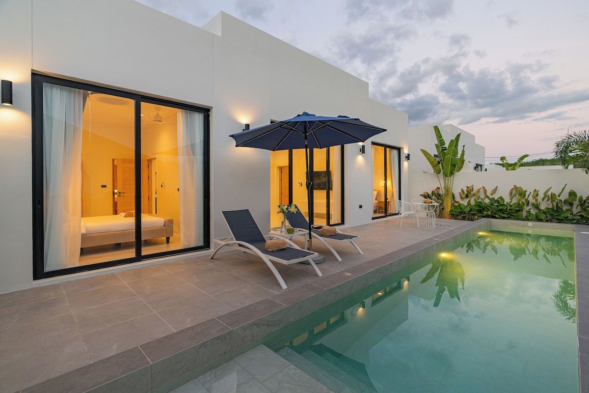 A modern hotel room with a large sliding glass door, a poolside area with lounge chairs and an umbrella, and a well-lit interior.
