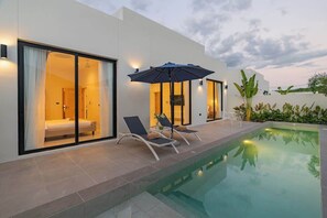 Un hôtel moderne doté d’une piscine, de chaises longues et d’un espace salon abrité.