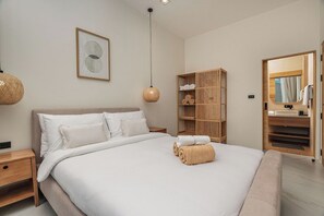 A modern bedroom with a large bed, a wooden wardrobe, a hanging light fixture, and a mirror.