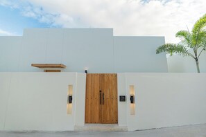 A modern building with a wooden double door, two wall-mounted lights, and a small bench above the door.