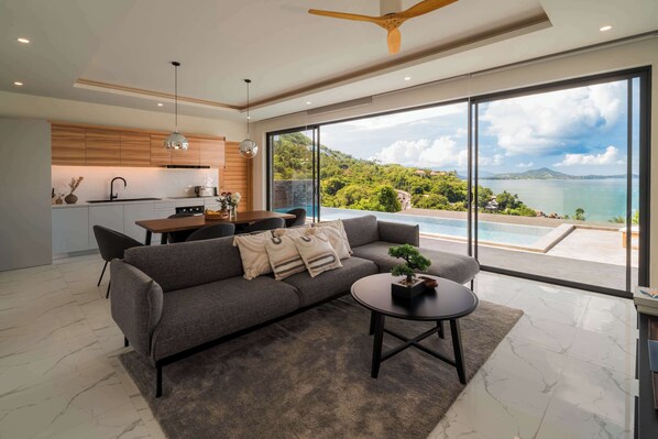 Una sala de estar moderna con sofá, mesa de centro y vistas a una piscina y montañas.