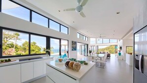 A modern kitchen with large windows, a central island, and a dining area with a view. - Staylar Luxury Seaview Pool Villa Maeva, Koh Samui (Koh Samui, Chaweng Noi)