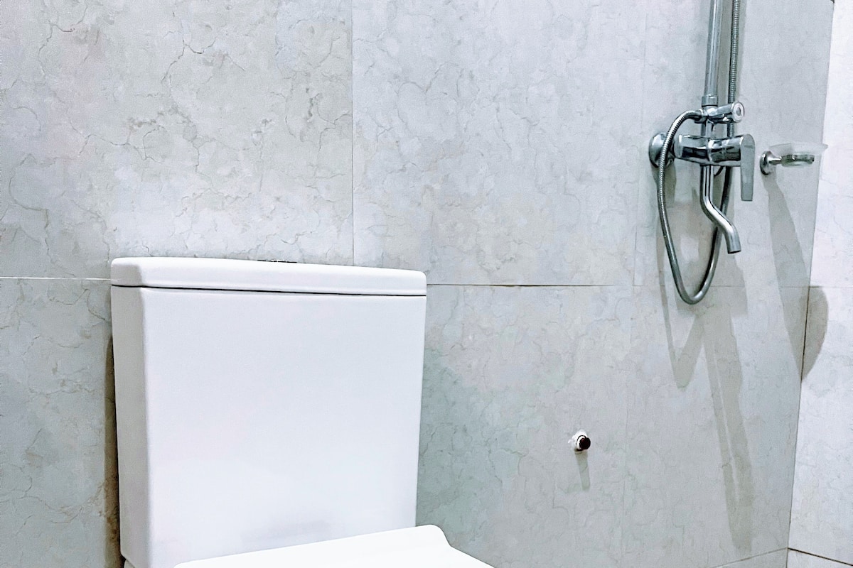 A white toilet with a closed lid, a showerhead, and a drain in a bathroom with tiled walls and floor.