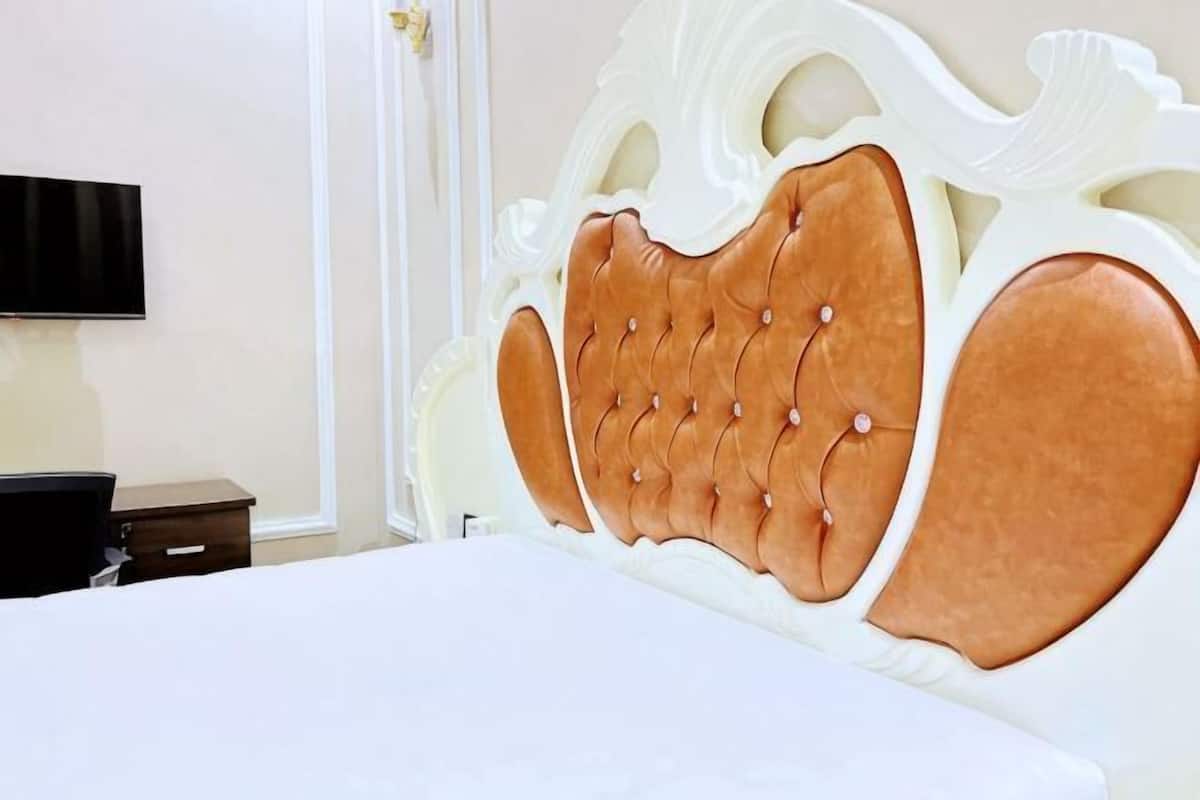 A bed with a tufted headboard, a flat-screen TV mounted on the wall, and a nightstand with a lamp.