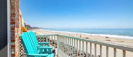 A balcony with turquoise chairs overlooking a beach.