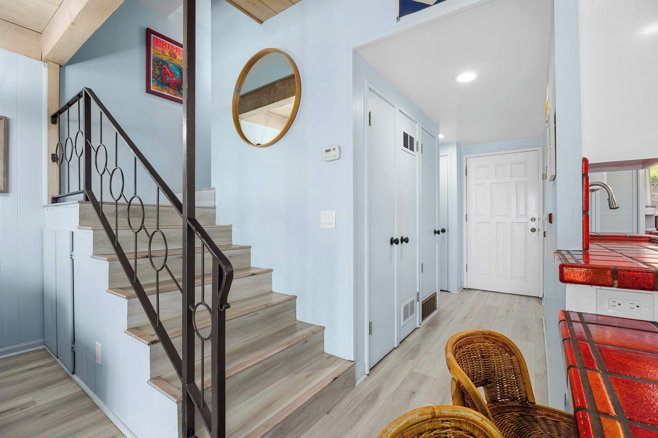 A staircase with a metal railing, a round mirror, and a door with a vent.