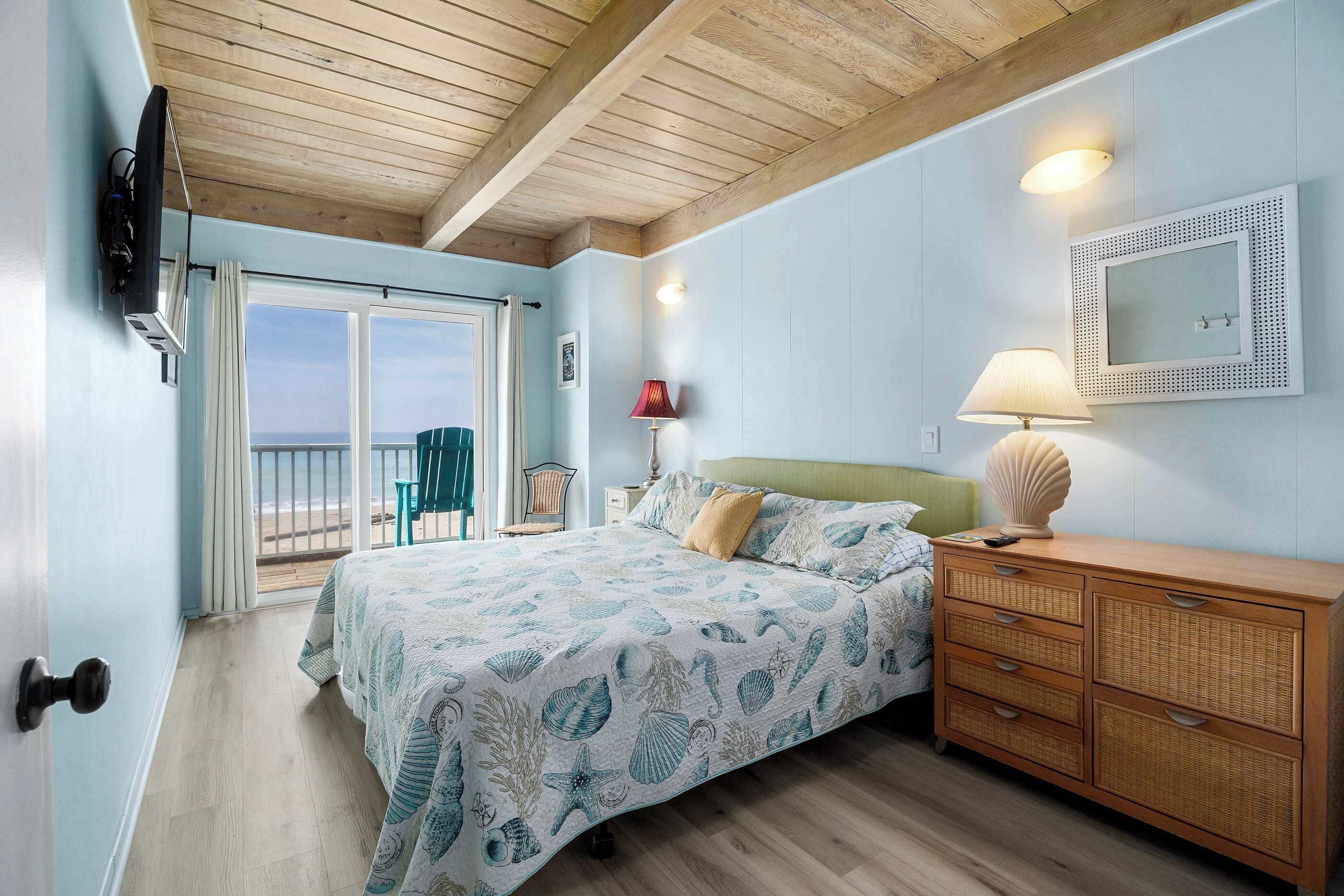 Une chambre à coucher avec un lit, une commode, un miroir et une vue sur la plage.