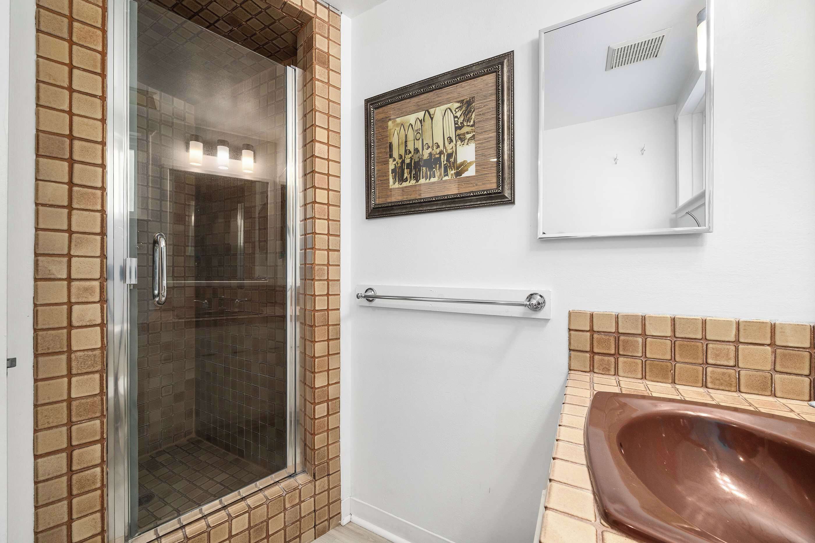 Un baño con cabina de ducha de vidrio, un cuadro en la pared, un lavamanos blanco y un perchero para toallas.