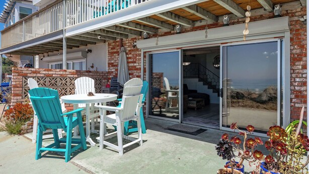 A patio with outdoor seating, a brick wall, and a sliding glass door leading to a covered area. - 1950's Beachfront Home - Stunning Views! (Aptos)