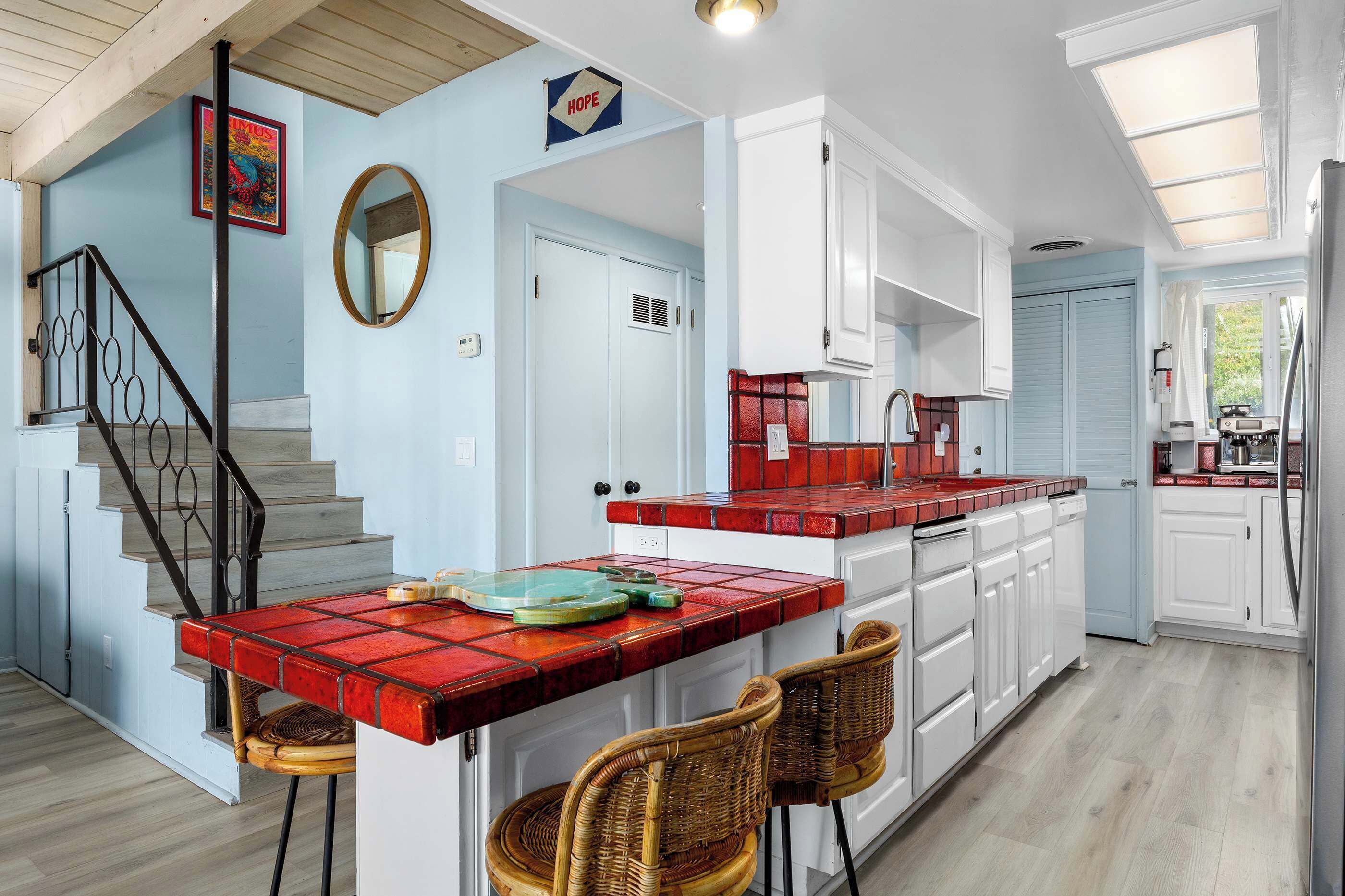 Una cocina con una isla de baldosas rojas y blancas, armarios blancos y una escalera de madera.