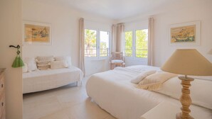 Une chambre avec un grand lit, un petit canapé, un fauteuil et une fenêtre avec des rideaux.