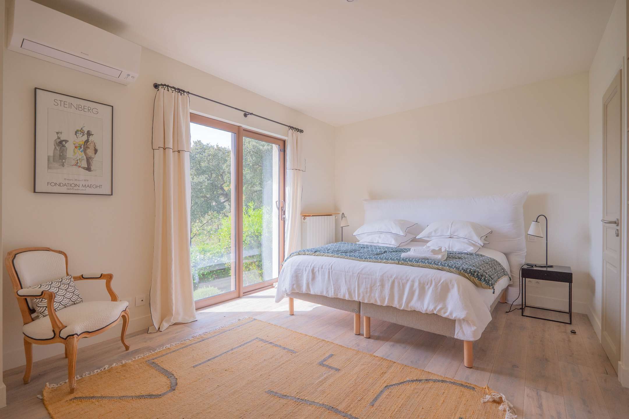 A bedroom with a bed, a chair, a nightstand, and a large window with curtains.