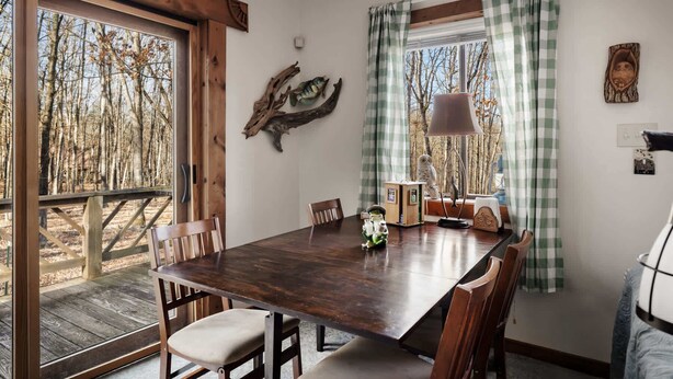 Un coin repas avec une table en bois, des chaises et une vue sur les arbres à travers de grandes fenêtres.
