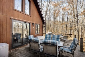 A wooden cabin with a deck, outdoor seating, and a grill.