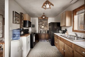 A compact kitchen with a brick wall, wooden cabinets, a refrigerator, a microwave, and a water dispenser.
