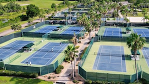 Oversigtsbillede af en tennisbane med flere baner, omgivet af palmer og grønt.