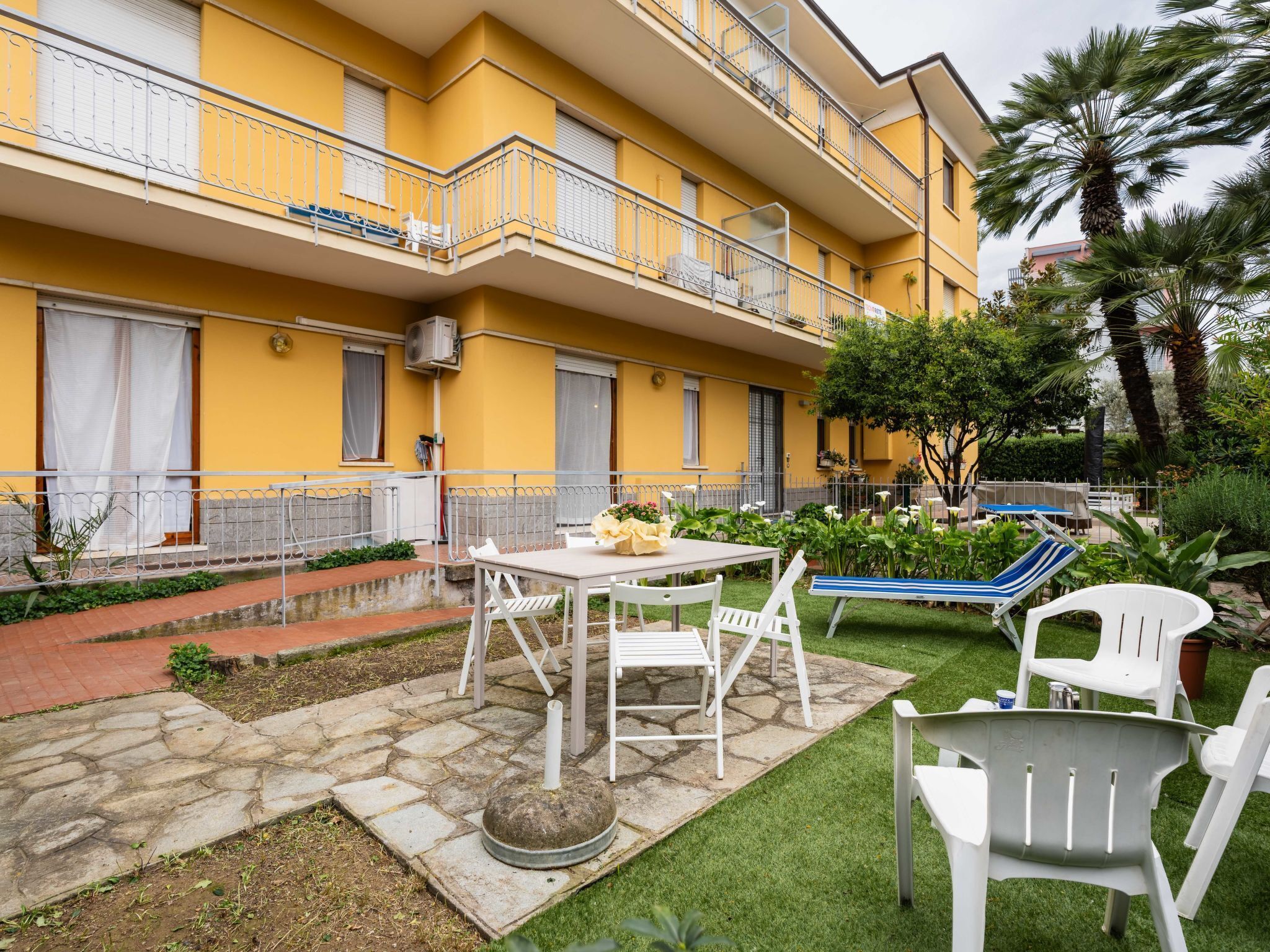 A yellow building with a balcony, a stone pathway, and outdoor seating.