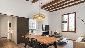 A modern living room with a wooden dining table, black chairs, a sofa, and a large window.