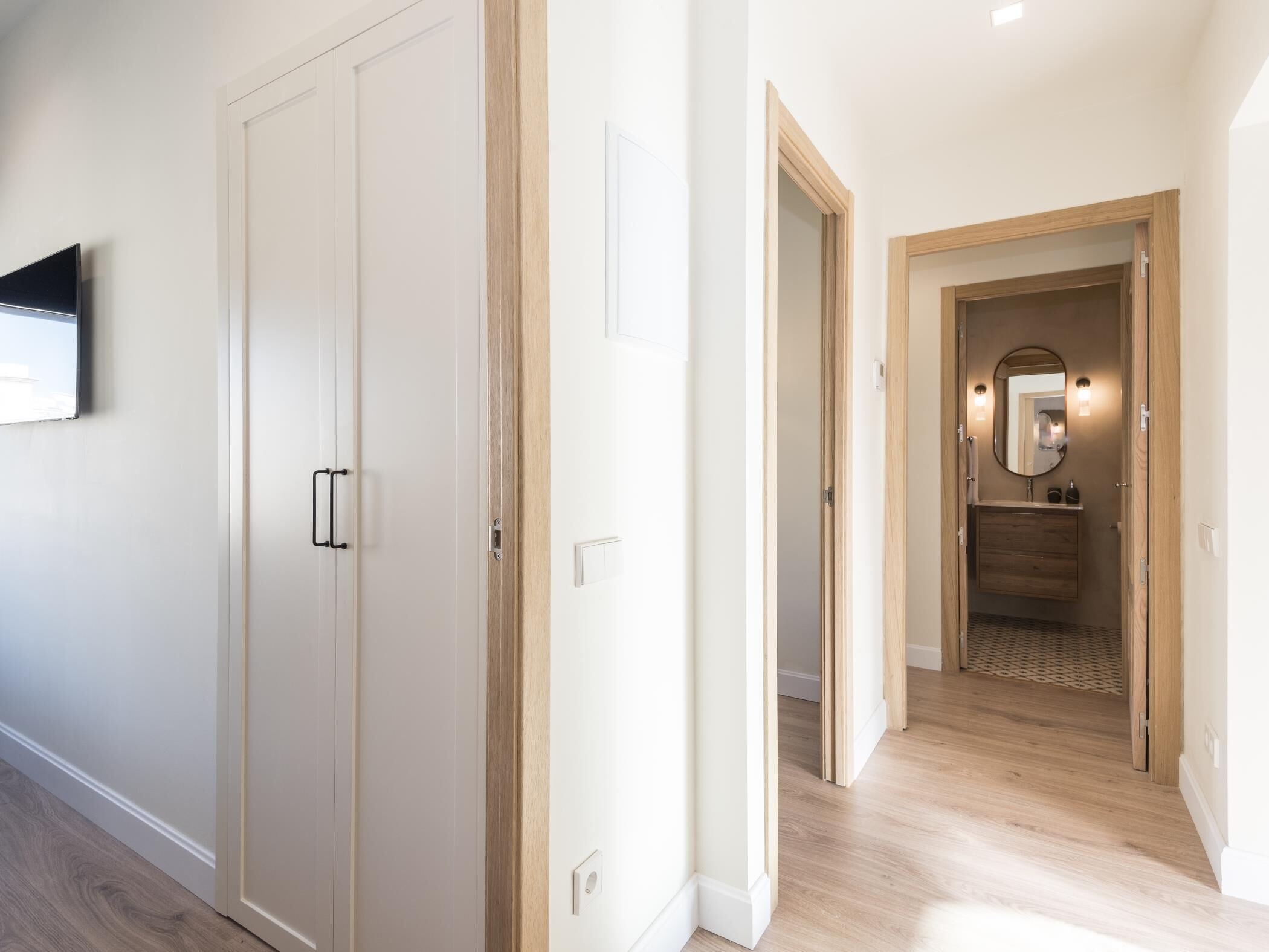 Un pasillo con suelo de madera, paredes blancas y una puerta de madera con pomo.