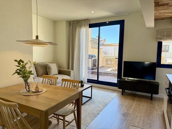 Una sala moderna con una mesa de comedor de madera, un sofá, un televisor y un balcón con vistas.