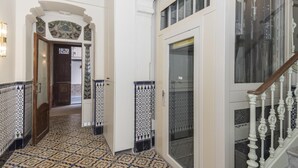 Un pasillo con baldosas de diseño, una puerta de madera y una escalera con barandilla blanca.