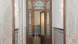 Un pasillo con puertas de madera decoradas, paredes con diseños y suelo de baldosas.
