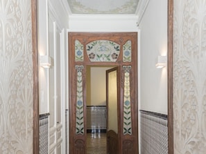 Un pasillo con puertas de madera decoradas, paredes con diseños y suelo de baldosas.