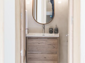 A bathroom with a wooden vanity, a white sink, and a mirror.
