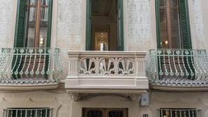 Fachada de edificio con detalles arquitectónicos ornamentales, incluyendo molduras decorativas y un balcón con barandilla de hierro forjado.