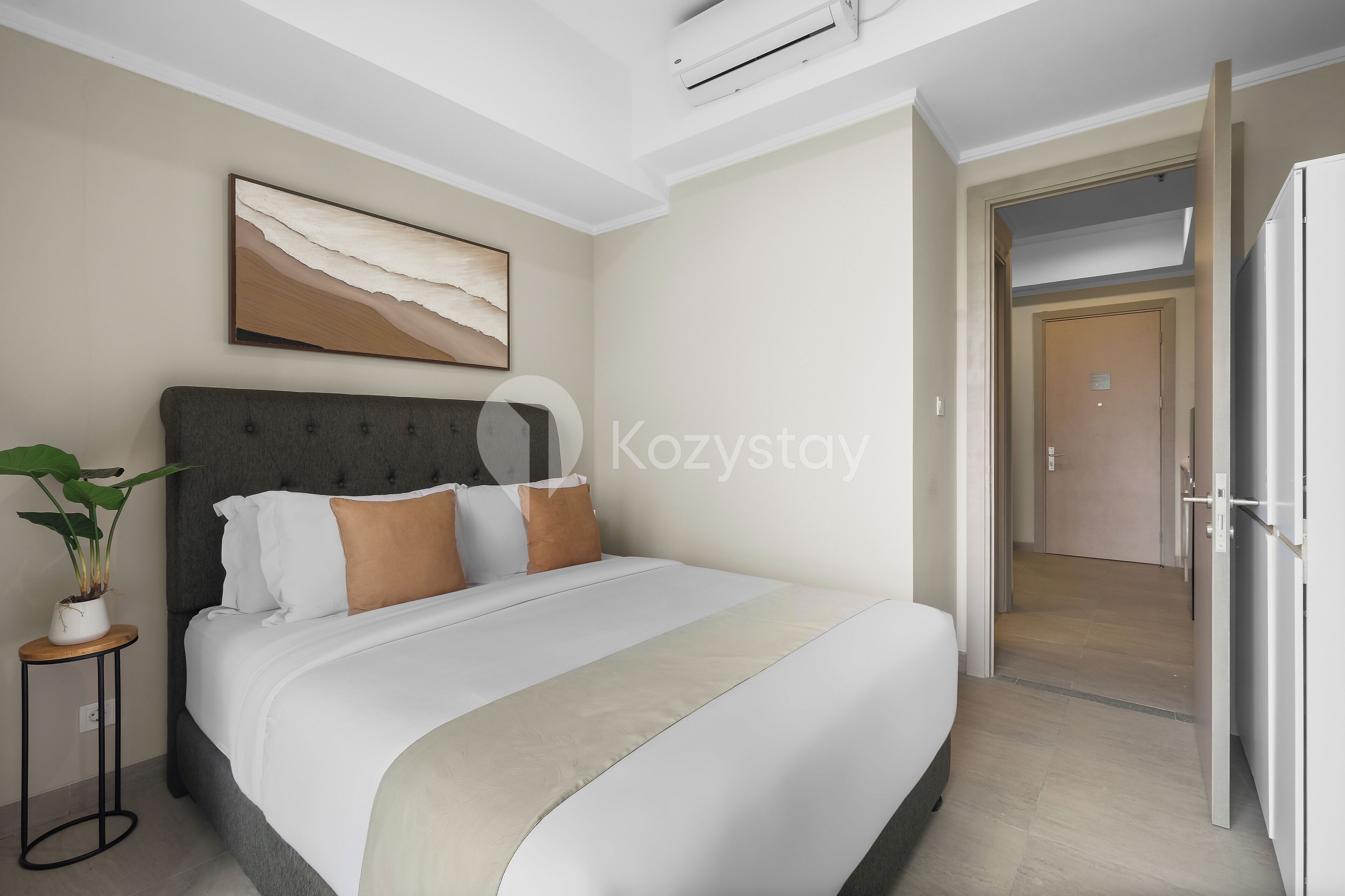 Ein modernes Hotelzimmer mit einem großen Bett, einer Topfpflanze, einem Gemälde und einer Tür zu einem anderen Raum.