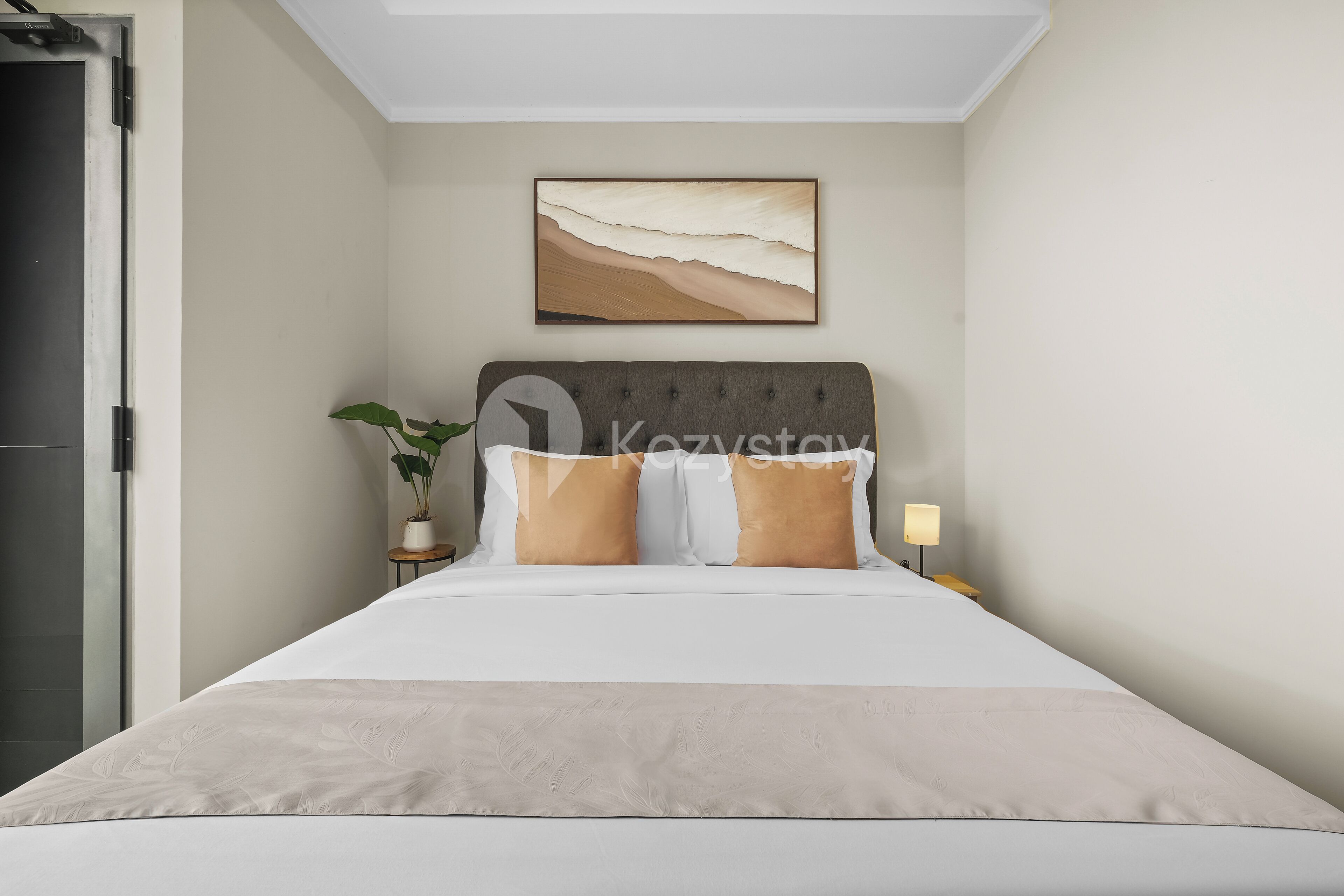 A neatly made bed with a headboard, a bedside table with a lamp, and a wall-mounted painting.