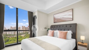 A modern hotel room with a large bed, a city view, and a simple nightstand.