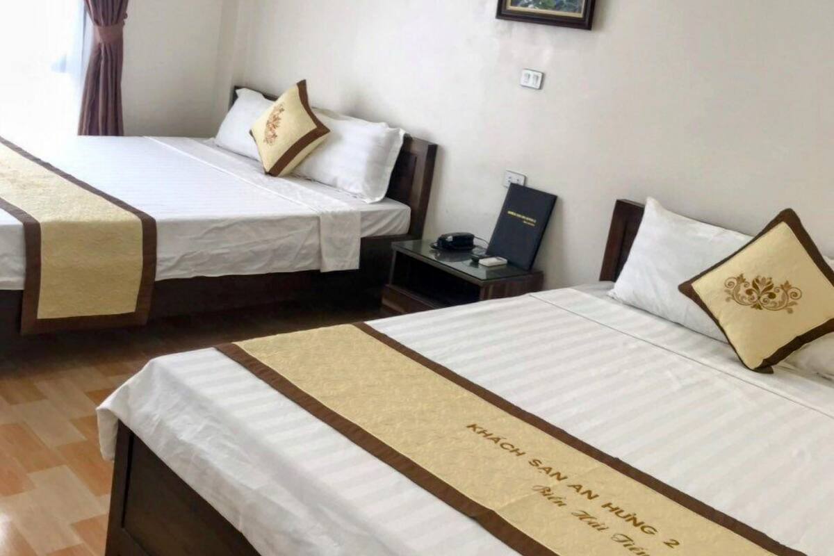 Habitación de hotel con dos camas, cada una con una alfombra beige y un cojín con diseño dorado. Hay un cuadro en la pared y una lámpara en la mesita de noche.
