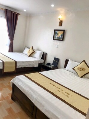 A hotel room with two beds, each with a beige runner and a pillow with a gold design. There is a framed picture on the wall and a lamp on the nightstand. - An Hung 2 Hotel Hai Tien -BAY LUXURY (Hoang Hoa)