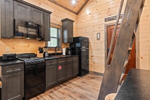 Modern kitchen with microwave, gas stove, and refrigerator, featuring wooden cabinets and a black countertop.