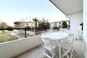 A balcony with a white table and chairs, a view of a residential area, and a clear sky.