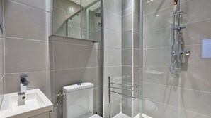 Et moderne badeværelse med et glasafskærmet brusebad, en hvid vask og et toilet.