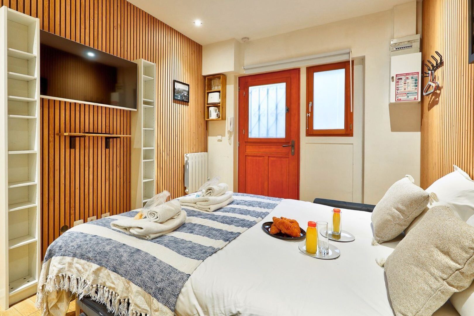 Ein Hotelzimmer mit Bett, Handtüchern, Frühstücksangeboten, einer Holzwand, einer Tür und einem Heizkörper.