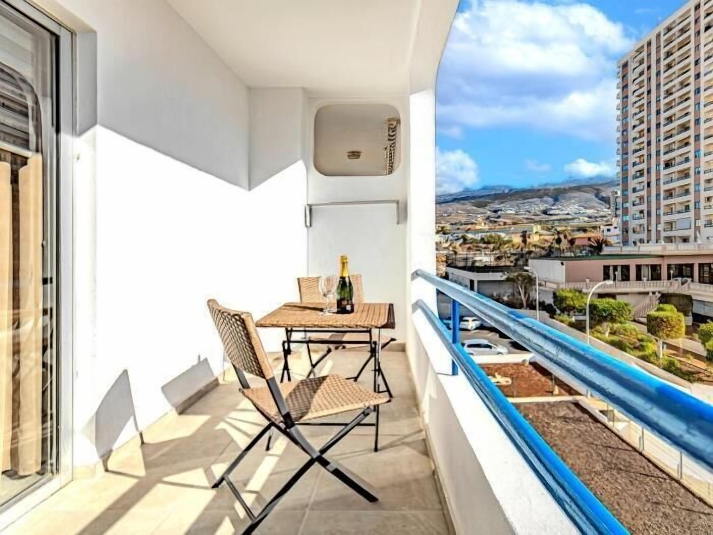 A balcony with a table and chairs, a bottle of champagne, and a view of a cityscape.